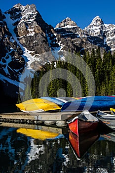 Bright canoes at moraine lake with snow covered rockies in background