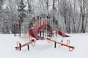 A bright children`s playground in the snow against the backdrop of the forest