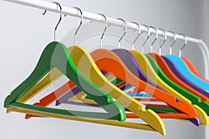 Bright clothes hangers on metal rack against light background, closeup