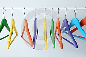 Bright clothes hangers on metal rail against light background