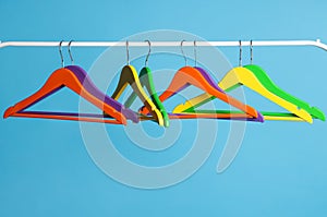 Bright clothes hangers on metal rail against light blue background