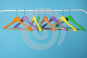 Bright clothes hangers on metal rail against light blue background