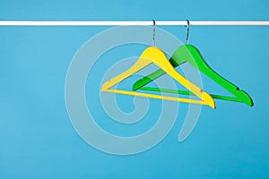 Bright clothes hangers on metal rail against light blue background. Space for text
