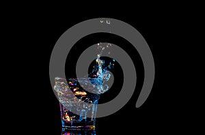 Bright cocktail in glass and splashing water on dark background