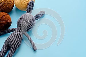 Bright color yarn clews with grey stuffed amigurumi bunny on the blue background. Concept of amigurumi toy making, handcrafting,