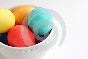 Bright colored Easter eggs nested in a white bowl.