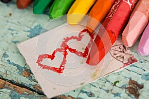 Bright colored pencils on an old blue green wooden background. Two red hearts painted on a slice of paper