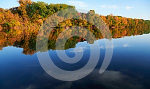 Bright colorful autumn forest landscape, trees near river and blue sky