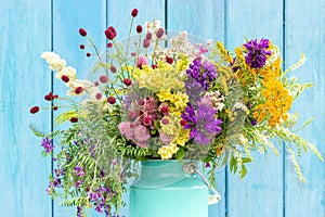 Bright colorful bouquet of wild flowers in starm tin can vase on background blue wooden boards. Template for postcard or your