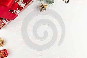 Colorful boxes tied with a red ribbon with gifts, golden cones and a Christmas tree branch on a background of white wood with gold