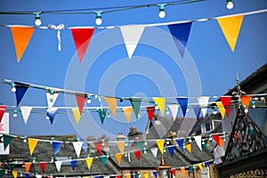 Bright colorful bunting or pennant flags hanging across pretty village street against blue sky for a traditional celebration,