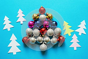 Bright colorful Christmas balls in the form of a Christmas tree and paper fir-trees on blue background