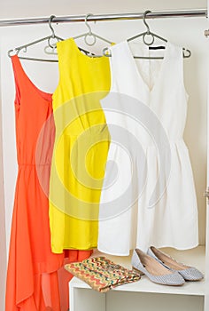 bright colorful dresses hanging on coat hanger, shoes and handbag in white wardrobe