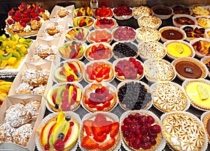 bright french pastries in a baker window, with chou, tropezienne, flan, eclair, and fruits tarts photo