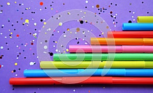 Bright colorful plastic drinking straws with multicolored sequins on a purple background