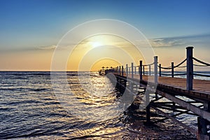 Bright and colorful sunrise over the pier and sea. Perspective view of wooden pier on the sea at sunrise with rocky