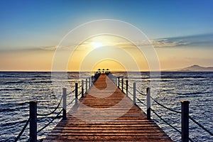 Bright and colorful sunrise over the sea and pier. Perspective view of wooden pier on the sea at sunrise with rocky