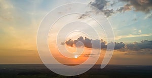 Bright colorful sunset sky with setting sun and vibrant clouds over dark landscape