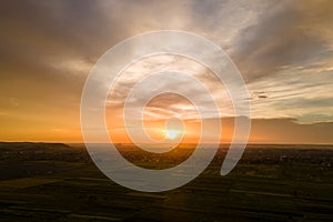 Bright colorful sunset sky with setting sun and vibrant clouds over dark landscape