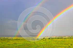 Bright colors of double rainbow rising from a meadow with dark rain clouds in the background
