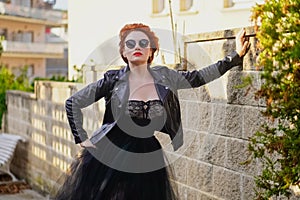 A bright confident beautiful red-haired woman in a black leather jacket, lace sexy dress and glasses