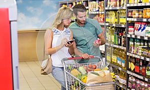 Bright couple buying food porducts and using notebook