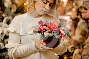 Bright creative flower arrangement decorated with golden Christmas tree decorations in woman`s hand.