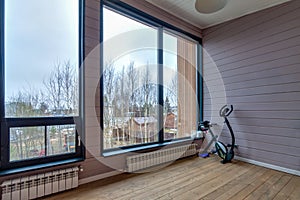 Bright dark room interior in wooden house with large window and exercise bike for sport and fitness in the corner. Scandinavian