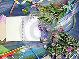 Bright decorative composition of art materials, notepad and flowers on a chalky blue background