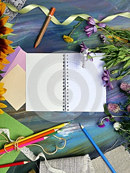 Bright decorative composition of art materials, notepad and flowers on a chalky blue background