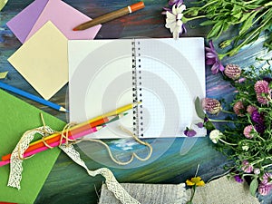 Bright decorative composition of art materials, notepad and flowers on a chalky blue background