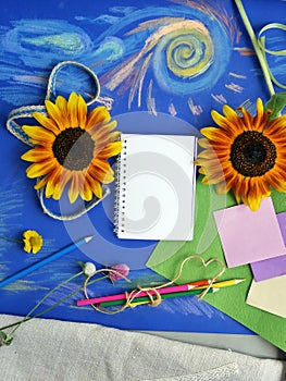 Bright decorative composition of art materials, notepad and flowers on a chalky blue background