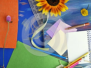 Bright decorative composition of art materials, notepad and flowers on a chalky blue background