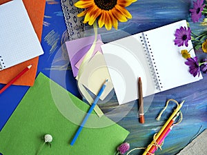 Bright decorative composition of art materials, notepad and flowers on a chalky blue background