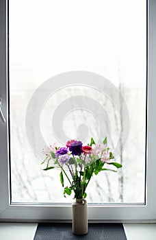 A bright delicate bouquet of flowers on the background of a white winter window.