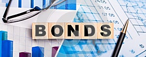 On the bright diagrams, glasses, a pen and wooden cubes with the word BONDS. Business concept