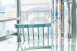 Bright dining area against a floor-to-ceiling window, with a blue traditional chair and glass table. Matching home decor in the