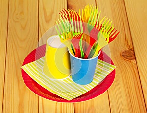 Bright disposable paper cups, plastic forks, plate on alight wood.