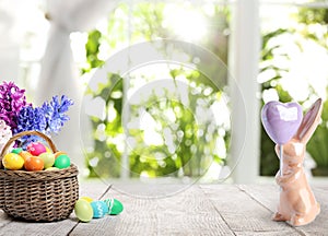 Bright Easter eggs in wicker basket and bunny figure on table
