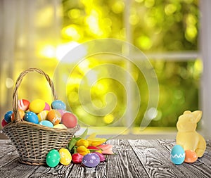 Bright Easter eggs in wicker basket and bunny figure on table