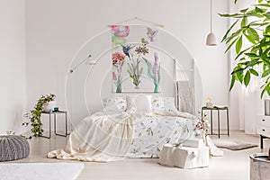 A bright eco friendly bedroom interior with a bed dresses in green plants pattern white linen. Fabric painted in flowers and birds