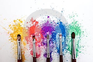 Bright eye shadows in different colors of the rainbow and brushes for cosmetics on a white background.