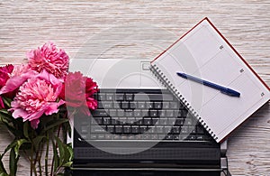 bright feminine workspace with open laptop computer, office supplies, fresh flowers, stylish clutch bag and other