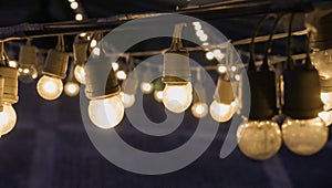 Bright festival garland light bulbs hanging over outdoor shopping area copy space