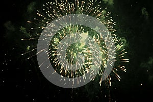 Bright fireworks with a green glowing center with green sparks and smoke, against the background of the night sky