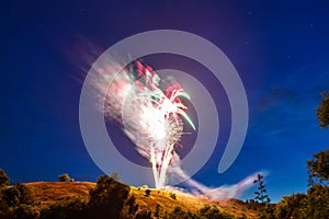 Bright fireworks over a hill in a natural landscape at night against a starry sky, a rural holiday landscape