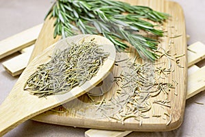 Bright fresh green and dried rosemary branches, twigs and leaves in a wooden spoon and on a board on light background.