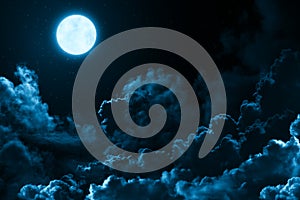 Bright full moon in the mystical midnight sky with stars surrounded by dramatic clouds. Dark natural background moon and clouds
