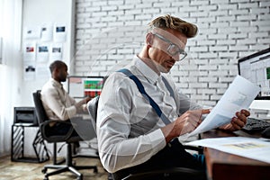 Bright future requires investment. Stylish businessman, trader looking through papers, while sitting by desk in front of