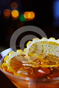 Bright glass of delicious alcoholic martini cocktail or lemonade with ice and a slice of orange on a table in a bar or restaurant